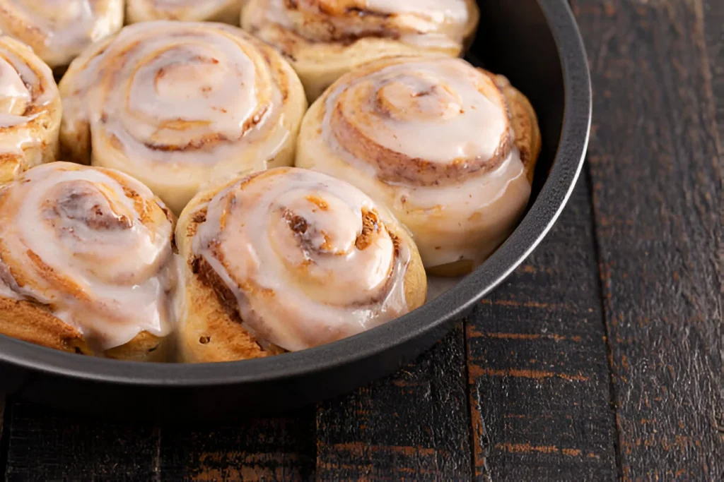 spreading frosting on cinnamon rolls in round dish.