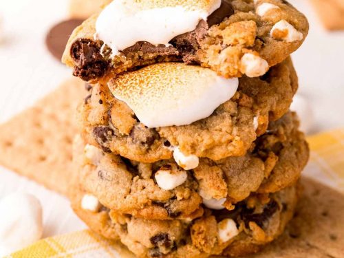 A plate of freshly baked Crumbl-inspired S’mores Cookies, featuring gooey mini marshmallows and dark chocolate chunks. The cookies are golden brown with a slightly crispy edge and soft center, showcasing the delicious melty chocolate and toasted marshmallows.