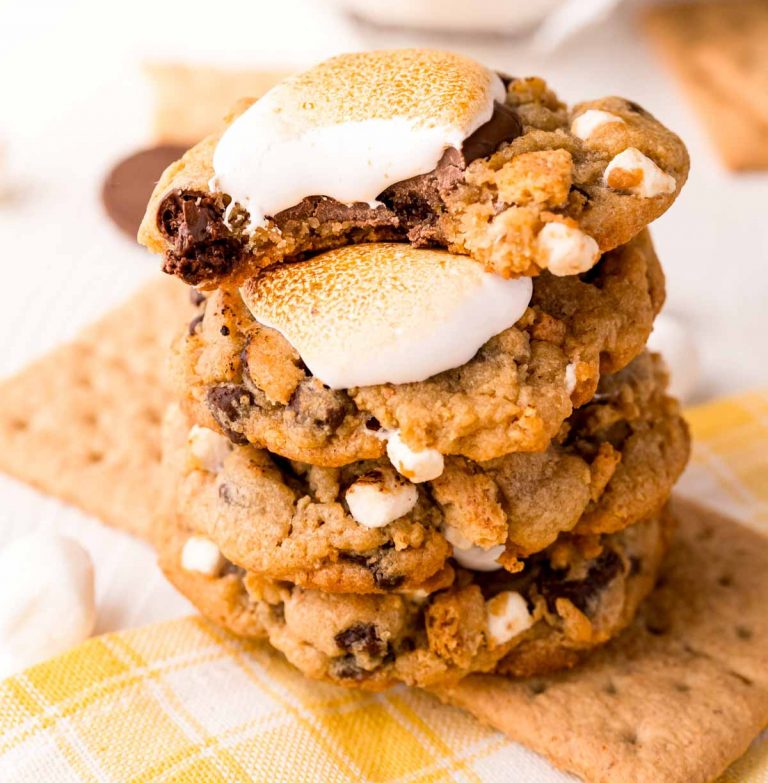 A plate of freshly baked Crumbl-inspired S’mores Cookies, featuring gooey mini marshmallows and dark chocolate chunks. The cookies are golden brown with a slightly crispy edge and soft center, showcasing the delicious melty chocolate and toasted marshmallows.