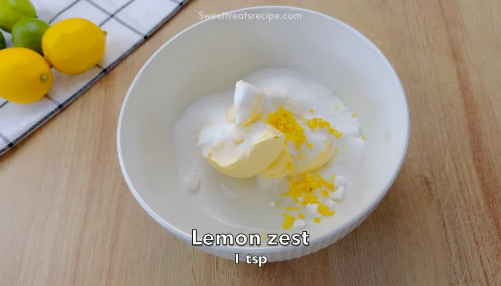 Mixing butter, sugar, and lemon zest in a bowl to prepare a lemon butter cake batter. Fresh lemons and limes on the side for flavor