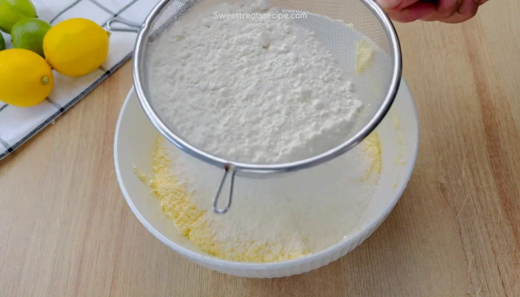 Sifting flour with a metal sieve into cake batter, with lemons and limes on a striped towel