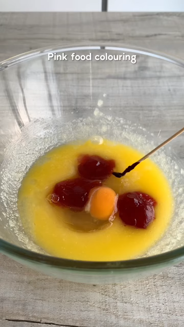 Mixing wet ingredients for strawberry shortcake cookies: melted butter, granulated sugar, strawberry jam, an egg, and pink food coloring in a glass bowl.