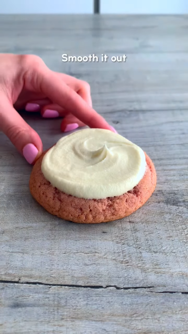 Frosting a strawberry shortcake cookie: spreading smooth cream cheese icing on a soft pink cookie. 