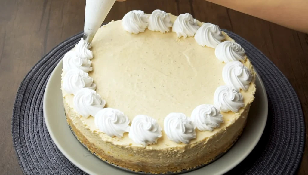 Close-up of a no-bake pumpkin cheesecake on a plate with whipped cream rosettes piped along the edge, set on a woven mat.