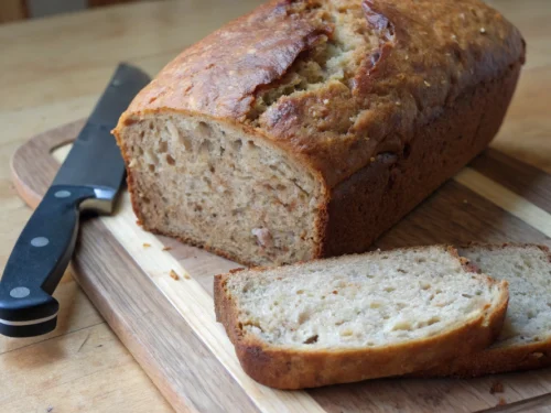 Freshly baked banana bread, sliced on a wooden cutting board.