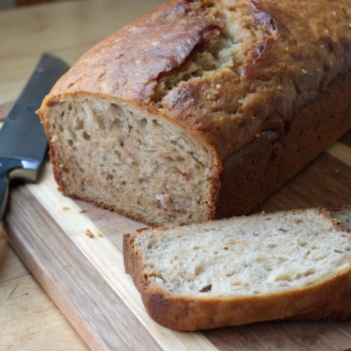 Freshly baked banana bread, sliced on a wooden cutting board.