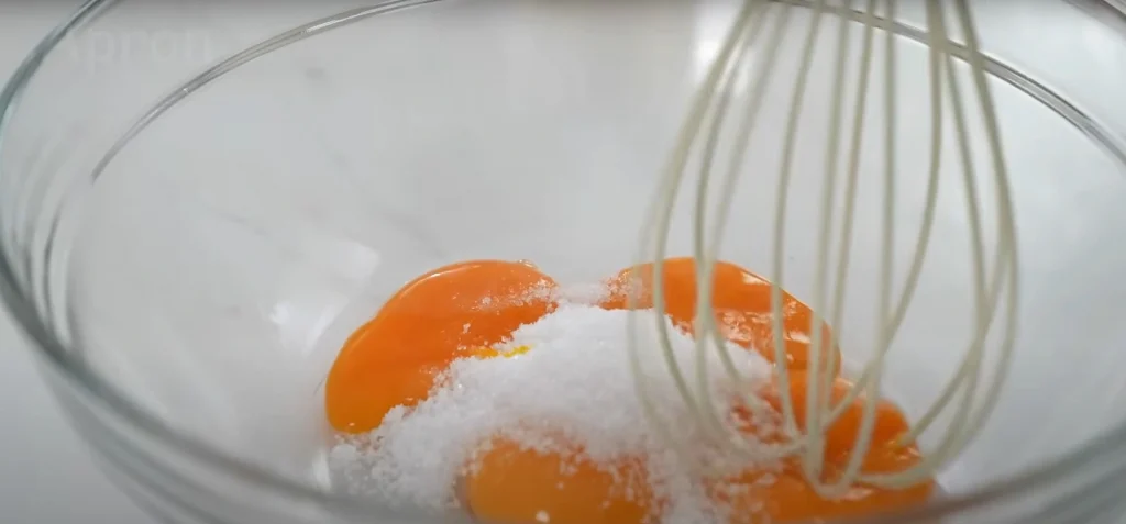 Egg yolks and sugar in a glass bowl with a whisk, preparing chiffon cake batter.