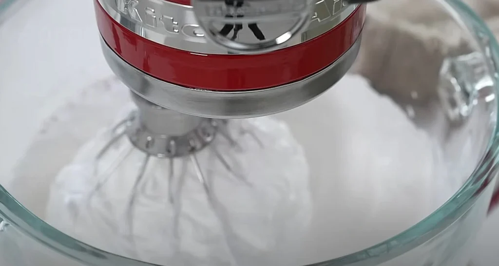 Egg whites being whipped to stiff peaks in a red stand mixer for chiffon cake preparation.